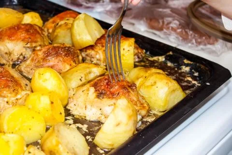 Fried chicken with potatoes on a baking sheet. A fork stuck in a fried piece  스톡 사진