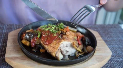Fried chicken with vegetables. The lunch process. The knife cuts the dish. Stock Photos