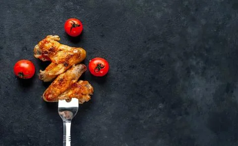 Fried chicken wing on fork with cherry tomatoes on dark background Stock-Fotos