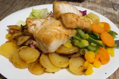 Fried cod with roasted potatoes and stewed vegetables Stock Photos