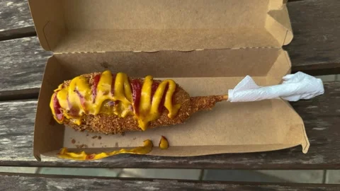 Fried corn dog with mustard and ketchup in cardboard box on wooden bench 스톡 동영상 338201349