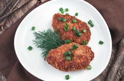 Fried cutlets with herbs in a white ceramic plate on a brown wooden background. Stock Photos