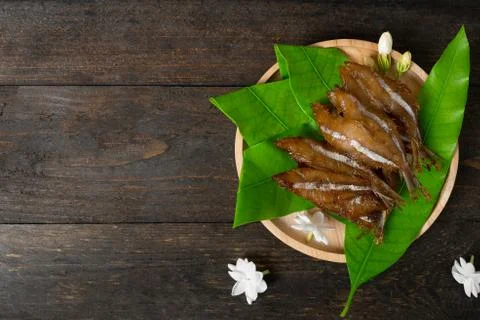 Fried dried fish on mango leaf in wooden dish on wooden table. Stock Photos
