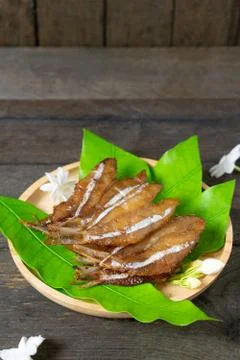 Fried dried fish on mango leaf in wooden dish on wooden table. Stock Photos