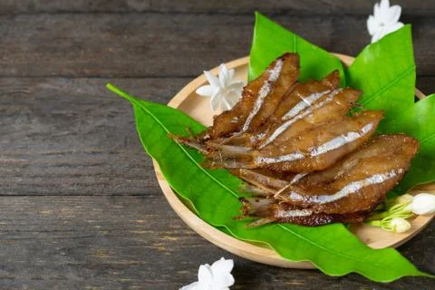 Fried dried fish on mango leaf in wooden dish on wooden table. Stock Photos