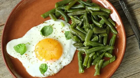 Fried egg and prepared green beans garnished with fresh basil leaves Stock Footage 340331737