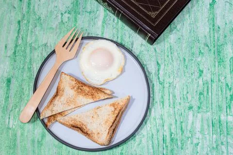 Fried egg bread in plate have book on green background. Stock Photos