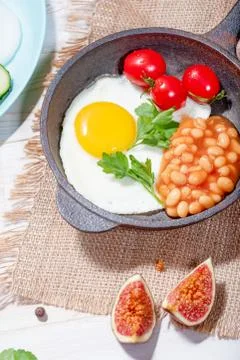 Fried egg in cast iron serving pan, cherry tomatoes, beans and vegetables Stock Photos