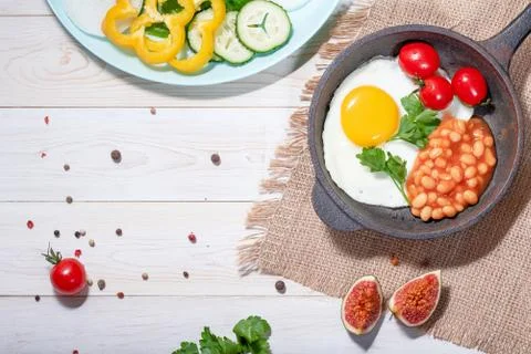 Fried egg in cast iron serving pan, cherry tomatoes, beans and vegetables Stock Photos