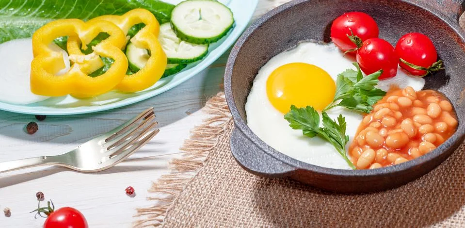 Fried egg in cast iron serving pan, cherry tomatoes, beans and vegetables Stock Photos