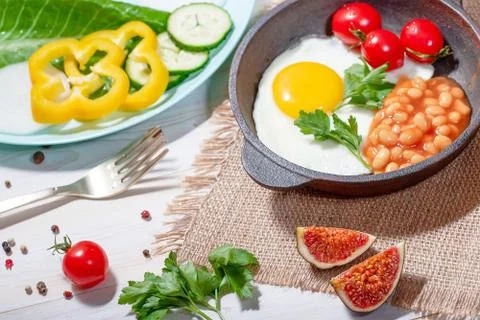 Fried egg in cast iron serving pan, cherry tomatoes, beans and vegetables Stock Photos