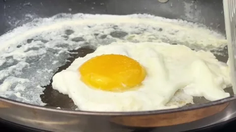 Fried egg cooking in a frying pan with butter and moving with a spatula Stock Footage 324943434