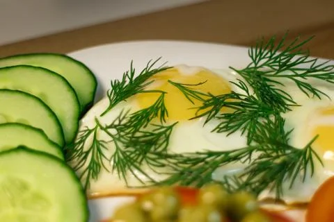 Fried egg. Example serving dill and slices cucumber on a white plate Stock Photos