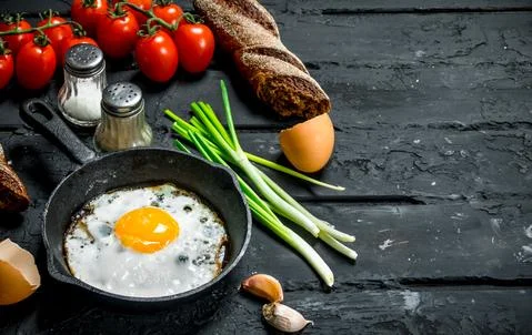 Fried egg in a pan with bread and tomatoes. Stock Photos