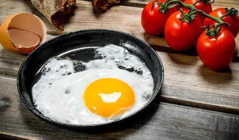 Fried egg in a pan with bread, tomatoes and green onions. Stock Photos