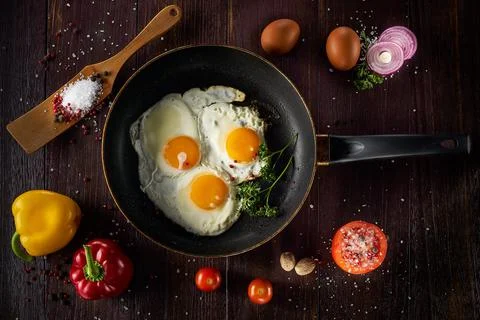 Fried egg in a pan with vegetables. On brown rustic background. Stock Photos