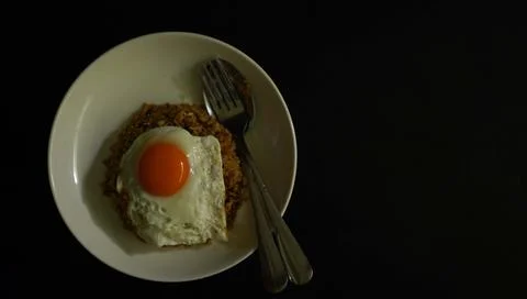 Fried egg placed on fried rice in a white plate black background Stock Photos