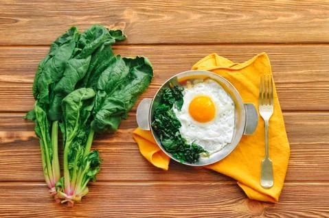 Fried egg with spinach on iron pan plate. Fried eggs healthy breakfast on wooden Foto stock