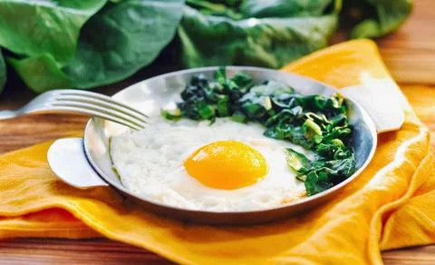 Fried egg with spinach on iron pan plate. Fried eggs healthy breakfast on wooden Stock Photos