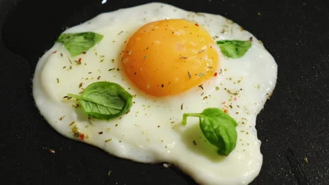 Fried egg sprinkled with spices and fresh basil leaves fried in a pan Stock Footage 340331638