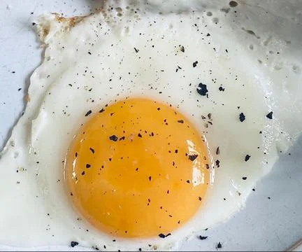 A Fried egg that is sunny side up and covered in pepper Stock Photos