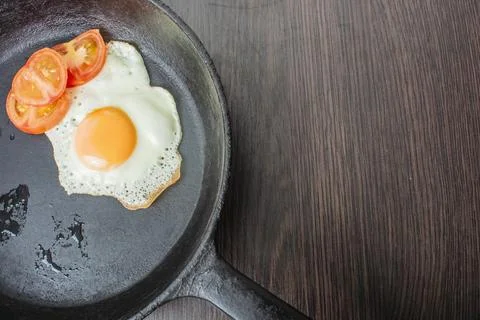 Fried egg with tomatoes in a cast-iron frying pan on a wooden table Stock Photos