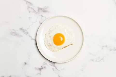 A fried egg on a white plate on a marble table Stock Photos