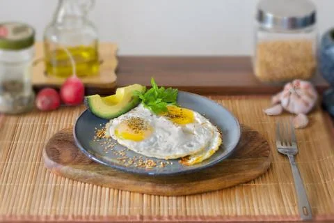 Fried eggs, accompanied by a slice of avocado Stock Photos