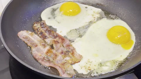 Fried eggs and bacon sizzling in pan detail 库存影片 333655601