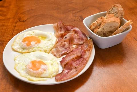 Fried Eggs and Crispy Bacon with Bread on a Wooden Table Stock Photos