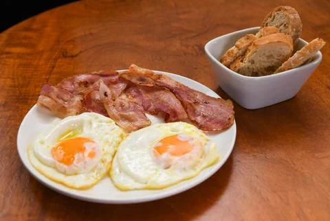 Fried Eggs and Crispy Bacon with Bread on a Wooden Table Stock Photos