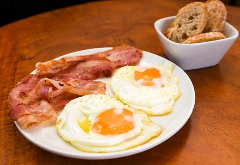 Fried Eggs and Crispy Bacon with Bread on a Wooden Table Stock Photos