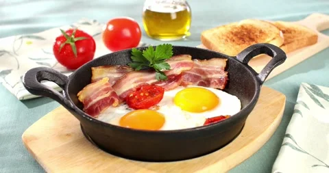 Fried eggs with bacon and tomatoes in a frying pan. breakfast on the table. Stock Footage 241370187