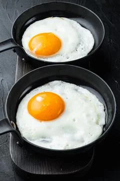 Fried eggs with bacon and vegetables in cast iron frying pan, on black backgr Stock Photos