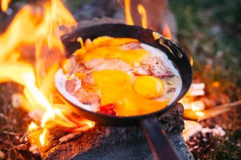 Fried eggs with bacon in a pan in the forest. Food at the camp. Fried egg wit Stock Photos