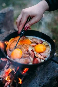 Fried eggs with bacon in a pan in the forest. Food at the camp. Fried egg wit Stock Photos