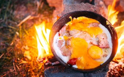 Fried eggs with bacon in a pan in the forest. Food at the camp. Fried egg wit Stock Photos
