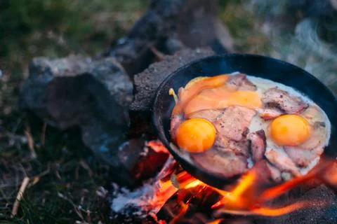 Fried eggs with bacon in a pan in the forest. Food at the camp. Fried egg wit Stock Photos
