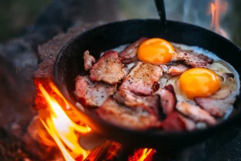 Fried eggs with bacon in a pan in the forest. Food at the camp. Fried egg wit Stock Photos