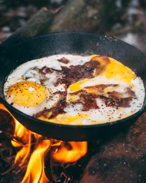 Fried eggs with bacon in a pan in the forest. Food at the camp. Fried egg wit Stock Photos