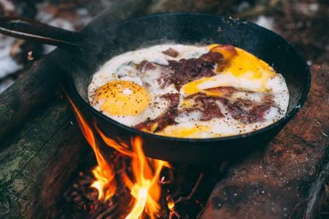 Fried eggs with bacon in a pan in the forest. Food at the camp. Fried egg wit Stock Photos