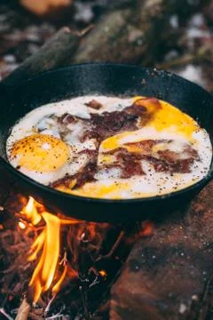 Fried eggs with bacon in a pan in the forest. Food at the camp. Fried egg wit Stock Photos
