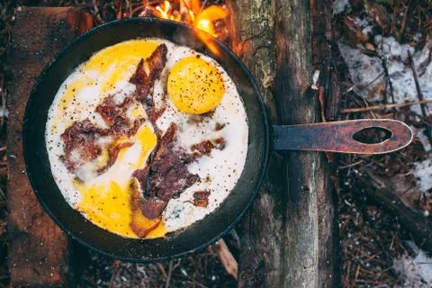 Fried eggs with bacon in a pan in the forest. Food at the camp. Fried egg wit Stock Photos
