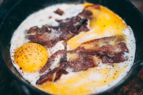 Fried eggs with bacon in a pan in the forest. Food at the camp. Fried egg wit Stock Photos