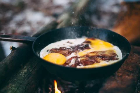 Fried eggs with bacon in a pan in the forest. Food at the camp. Fried egg wit Stock Photos