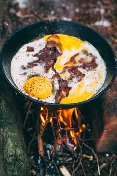 Fried eggs with bacon in a pan in the forest. Food at the camp. Fried egg wit Stock Photos