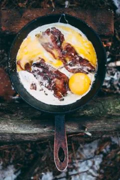 Fried eggs with bacon in a pan in the forest. Food at the camp. Fried egg wit Stock Photos