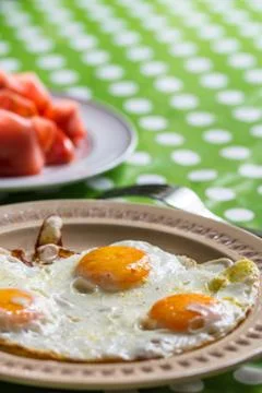 Fried eggs for breakfast with tomato in background Stock Photos