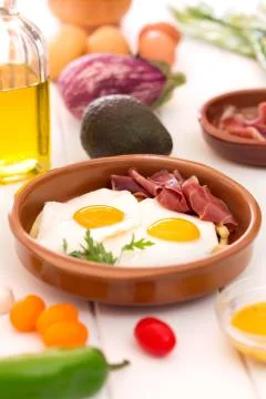 Fried eggs in a ceramic cup with spanish jamon for breakfast on a white backg 写真素材