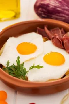 Fried eggs in a ceramic cup with spanish jamon for breakfast on a white backg 写真素材